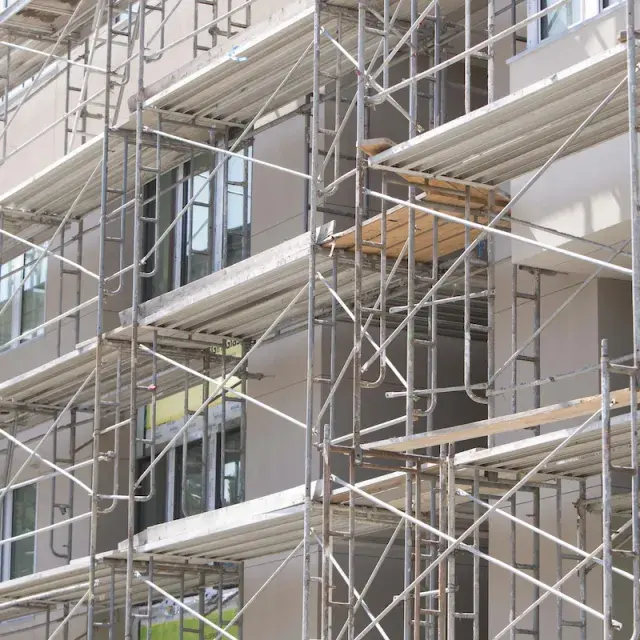 Scaffolding surrounds a multi-story residential building under construction, with partially installed windows and exterior finishes visible.