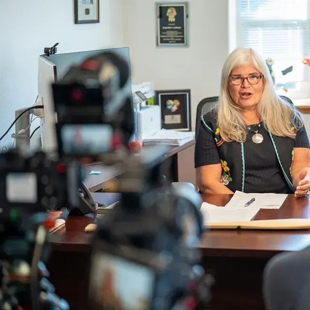 A women sitting at a desk recording while being video recorded