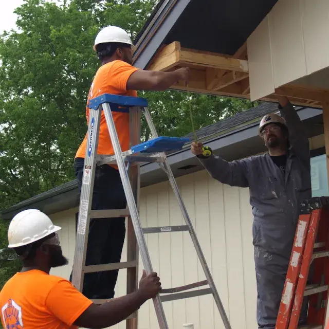 Men in orange clothing on ladders working on building