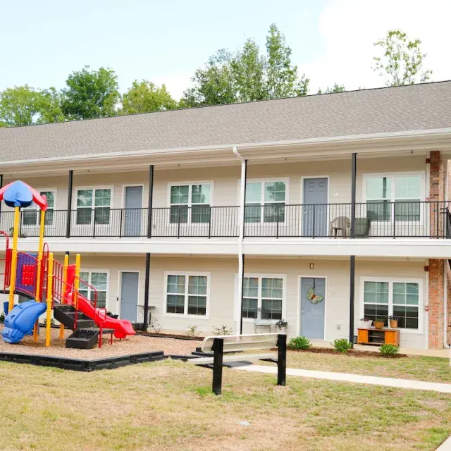Two story brick and beige siding apartment building with playground in front