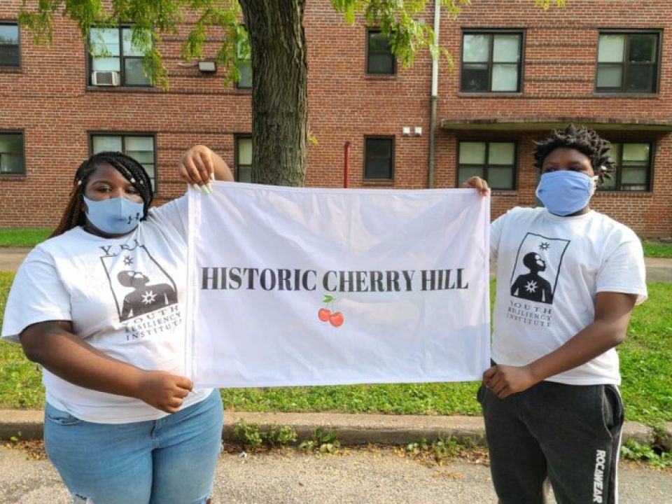 Two young people wearing protective masks hold up a sign that reads "Historic Cherry Hill"