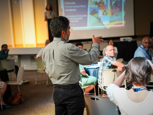 Speaker talks to people sitting at round tables in a large meeting room