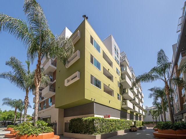 A closeup of the apartments at Movietown, a lime-colored building with palm trees lining the sidewalks
