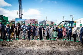 A line of people with green hard hats standing and holding matching green shovels at a groundbreaking ceremony