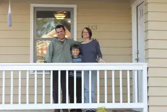 A family of three standing on a the front porch smiling